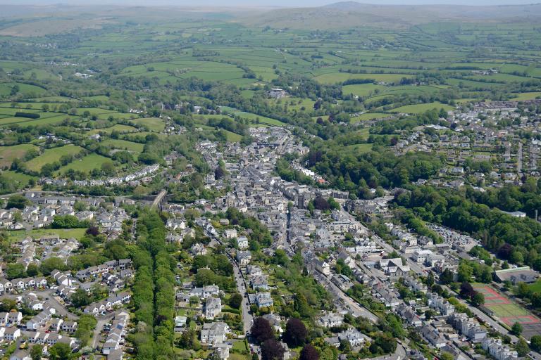 An aerial view of Tavistock, showing the town on a sunny day, nestled in green fields with Dartmoor visible in the distance.